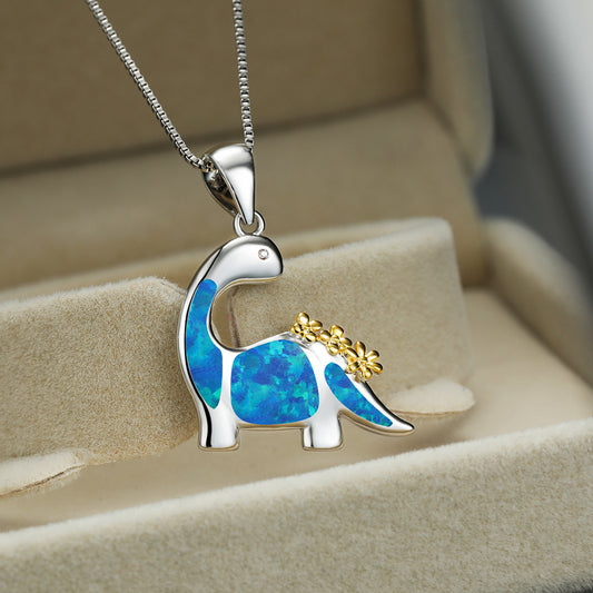 Dinosaur-shaped pendant with blue opal and gold accents on a chain, displayed in a jewelry box.