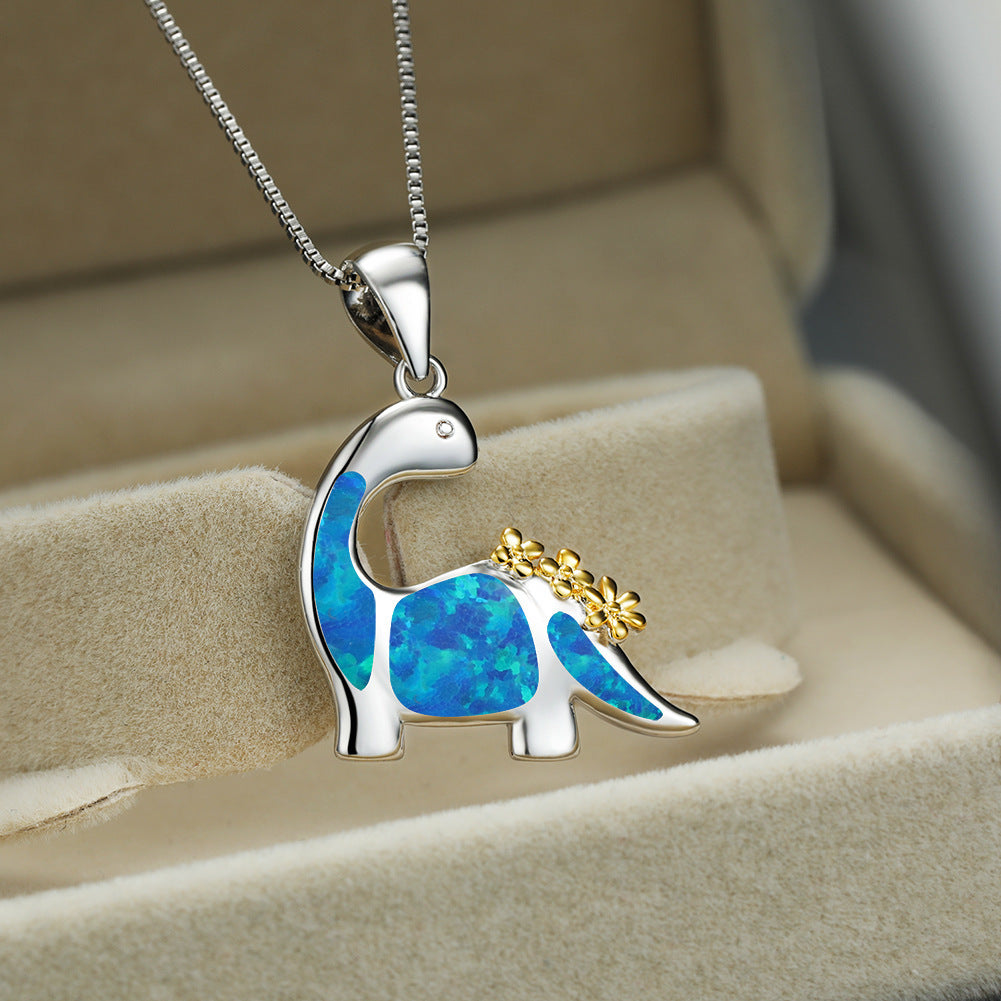 Dinosaur-shaped pendant with blue opal and gold accents on a chain, displayed in a jewelry box.