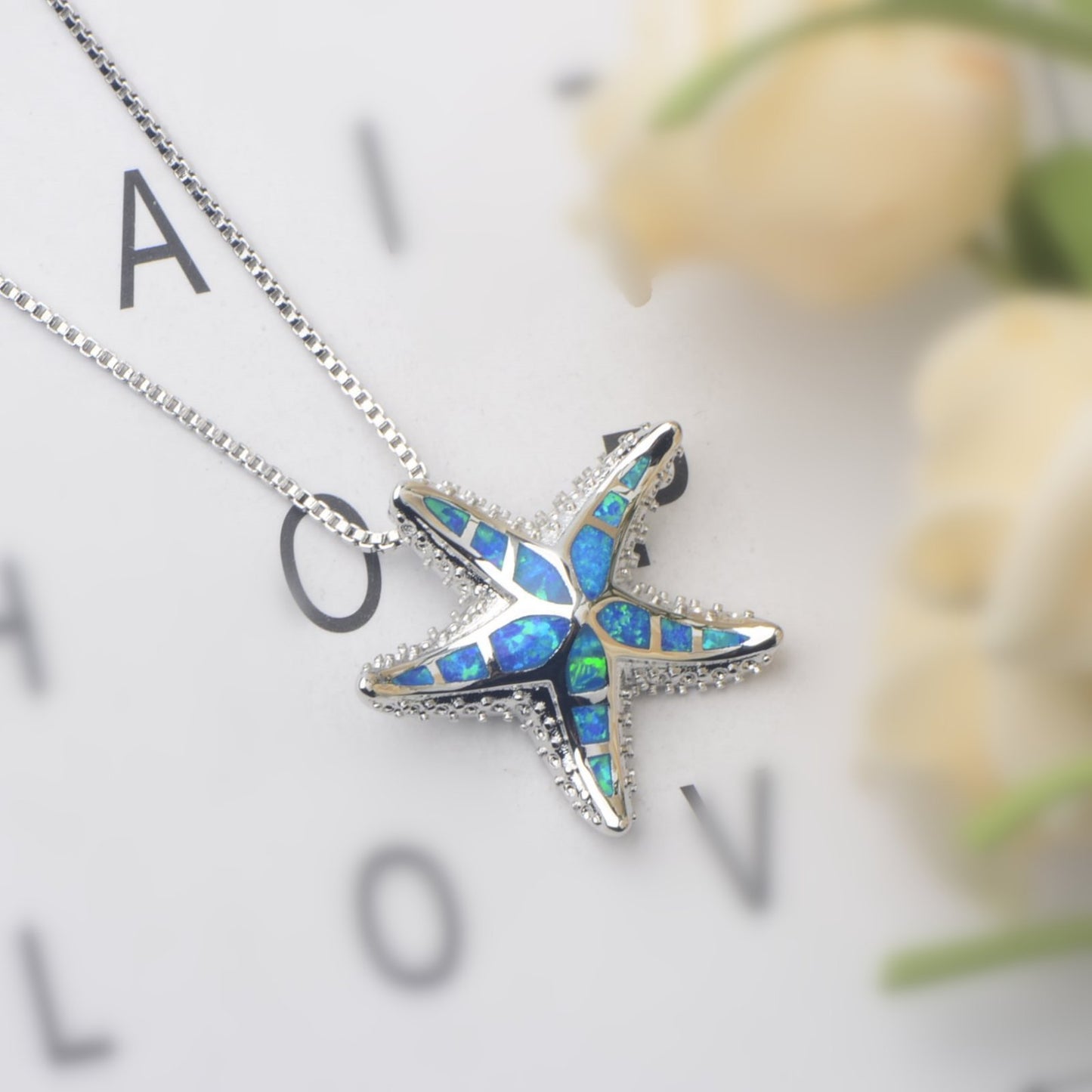 Starfish-shaped pendant with blue and green opal inlay on a silver chain against a blurred background.